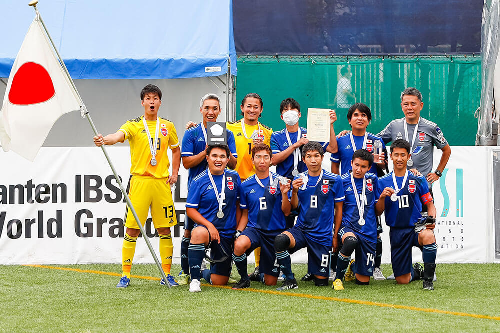 写真：全員が銀メダルを首から下げ、日本国旗とともに写るブラサカ日本代表チーム