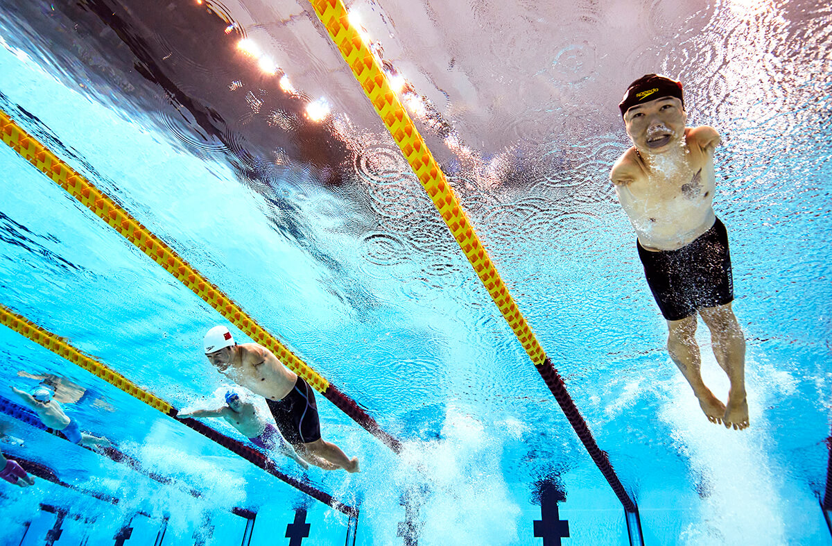 写真：水中の下から上に向けて、中国の鄭濤（チェン・タオ）選手や他の選手たちが泳ぐところを捉えたショット。ゴーグルをしていないチェン選手の目がしっかりと見開いている。