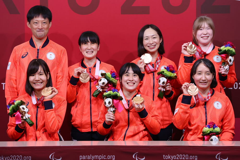 写真：銅メダルとメダリストに送られる花のブーケを手に笑顔のゴールボール女子チームと市川監督