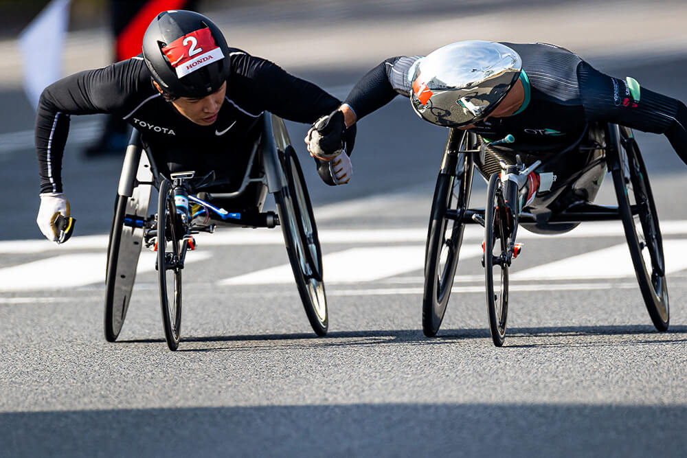 写真：第40回記念大分国際車いすマラソン・マルセル・フグ選手と鈴木朋樹選手。フグ選手が先頭を維持し、二人の好記録となった。