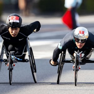 サムネイル写真：第40回記念大分国際車いすマラソン・車道のコース上で並走するマルセル・フグ選手と鈴木朋樹選手