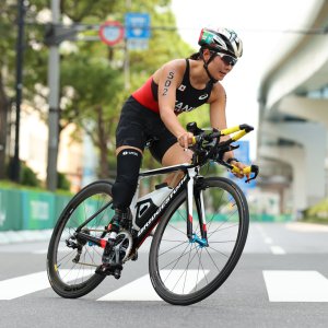 サムネイル写真：パラトライアスロン・谷真海選手が競技用自転車に乗って、横断歩道を走り抜けるシーン