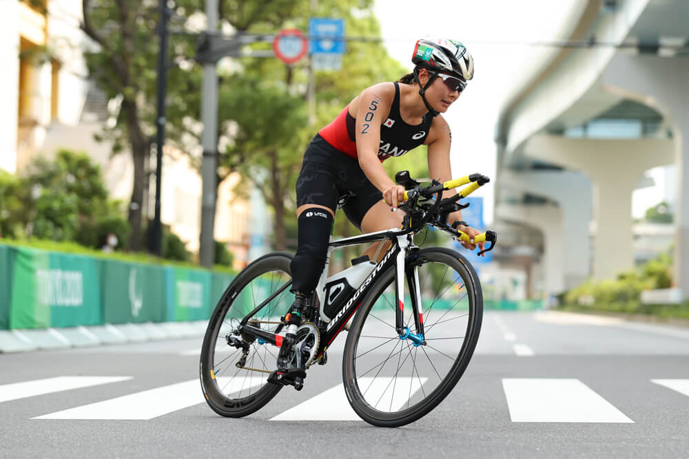 写真：パラトライアスロン・谷真海選手が競技用自転車に乗って、横断歩道を走り抜けるシーン