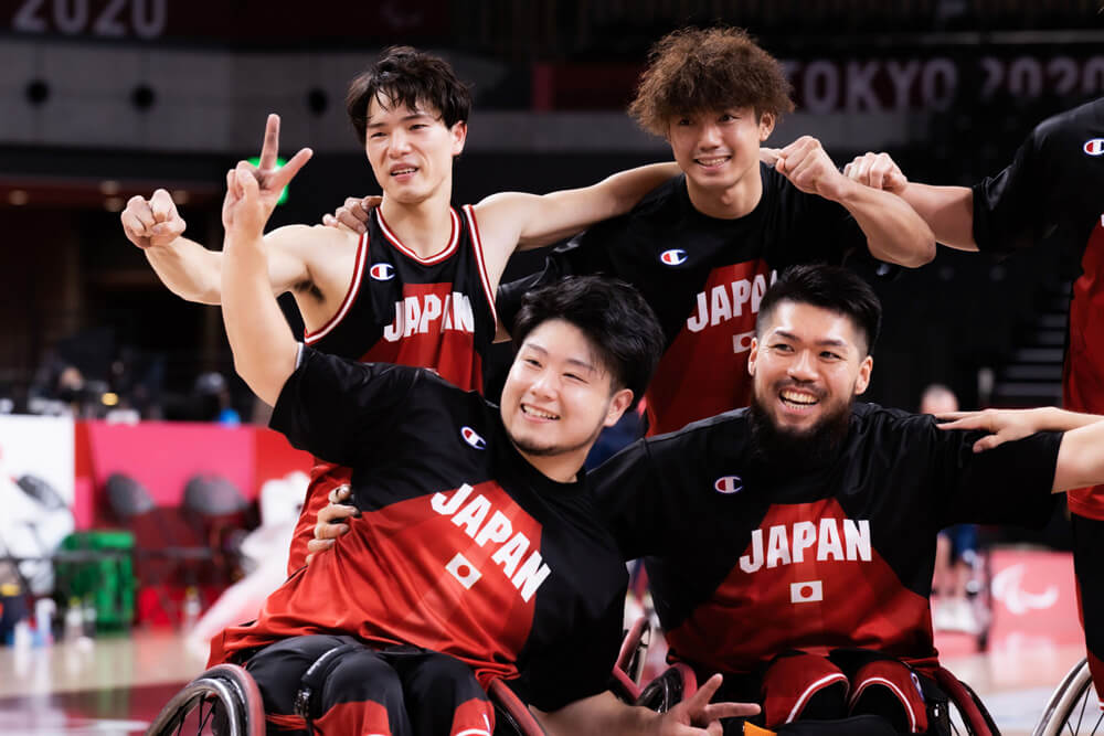 写真：東京2020パラリンピック車いすバスケットボール日本代表・川原凜選手が笑顔でピースをしながら、他の日本人選手たちと集合写真の撮影に応じている様子